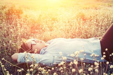 Happy hipster woman lying down on dandelion field close her eyes feeling comfortable
